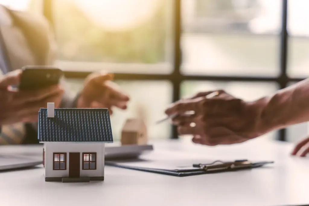 Two people looking over paperwork with a miniture house on the desk.