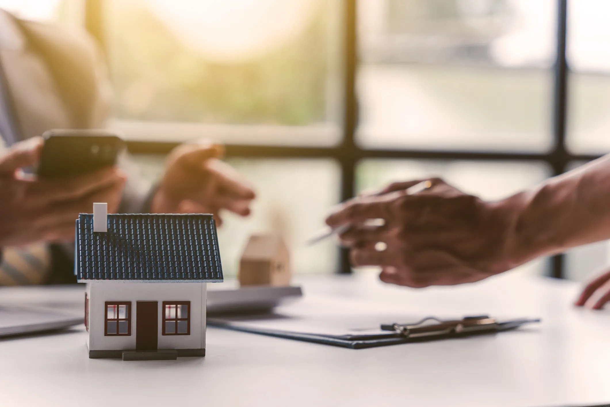 Two people looking over paperwork with a miniture house on the desk.
