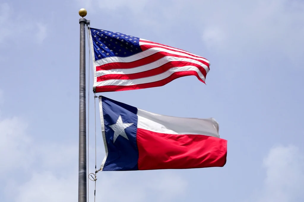 The flag of Texas and the American flag flying on a flag post.