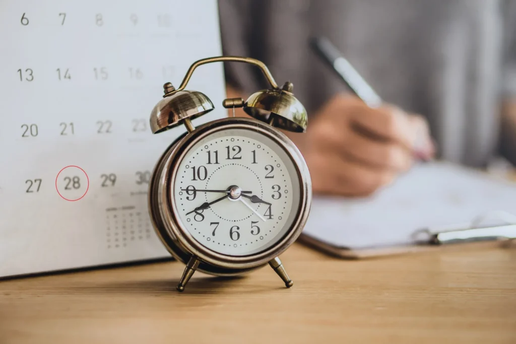 A calendar and an alarm clock set on a table, while a person fills out paperwork.