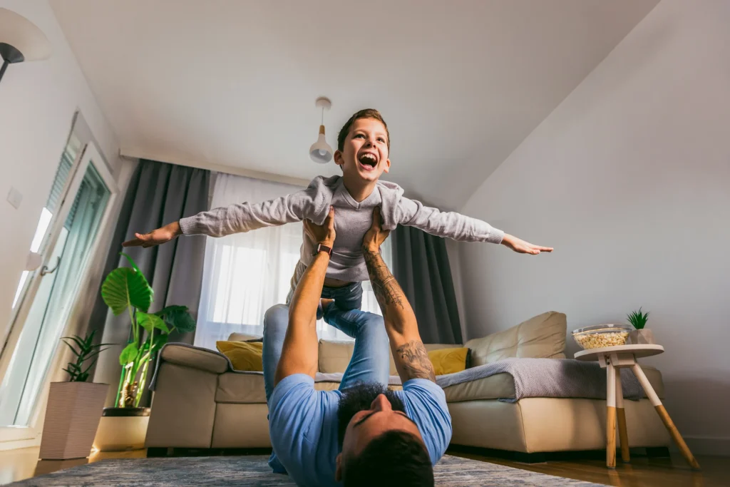 A dad holding up his son with his arms out.