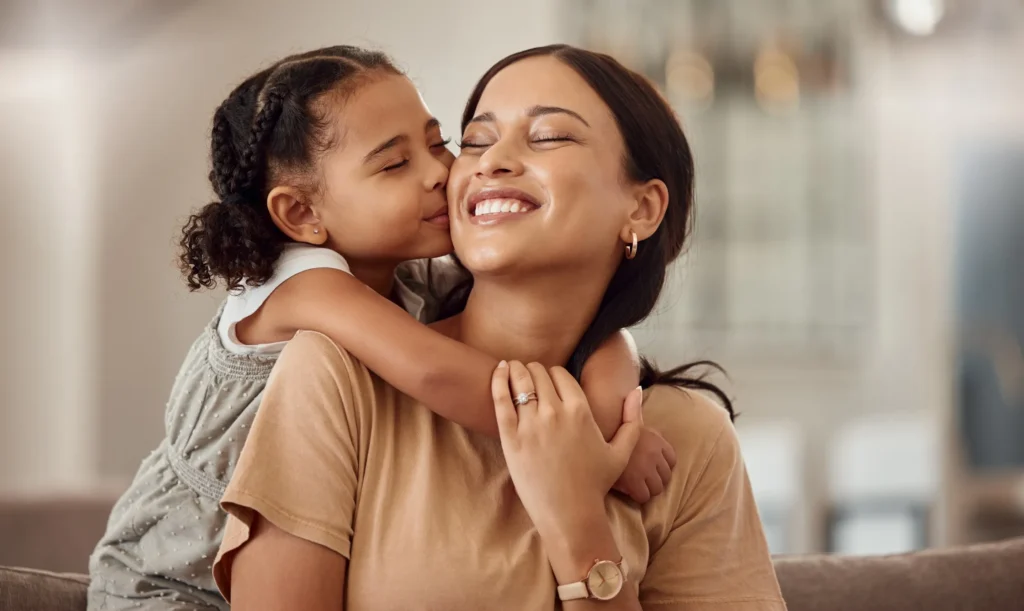 A daughter hugging and giving her mom a kiss on her cheek.
