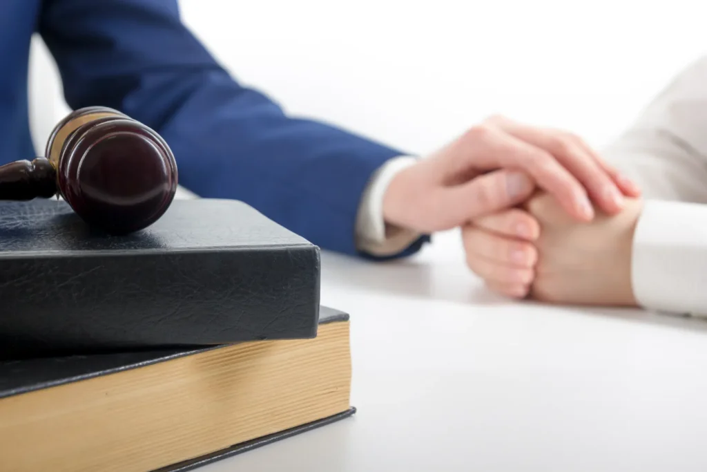 An attorney putting his hand over his clients folded hands with a gavel on top of books.