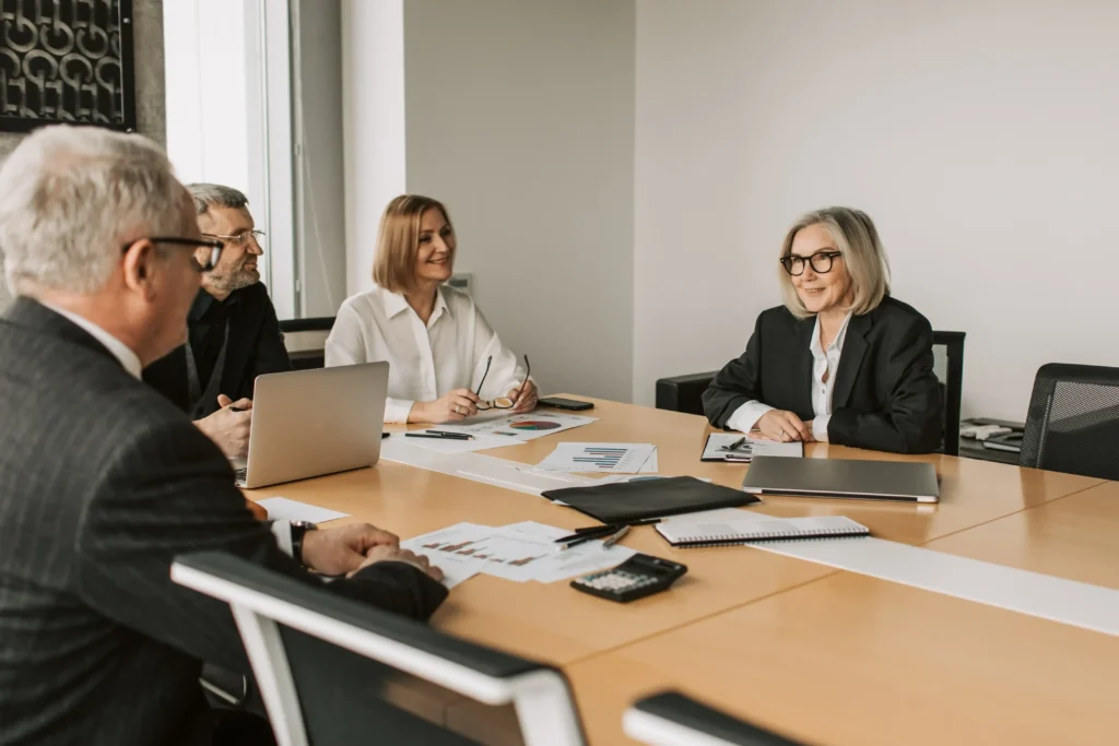Group of professionals in business attire having a meeting around a conference table with charts and documents, representing legal and governance discussions for Texas small and medium-sized businesses (SMBs).