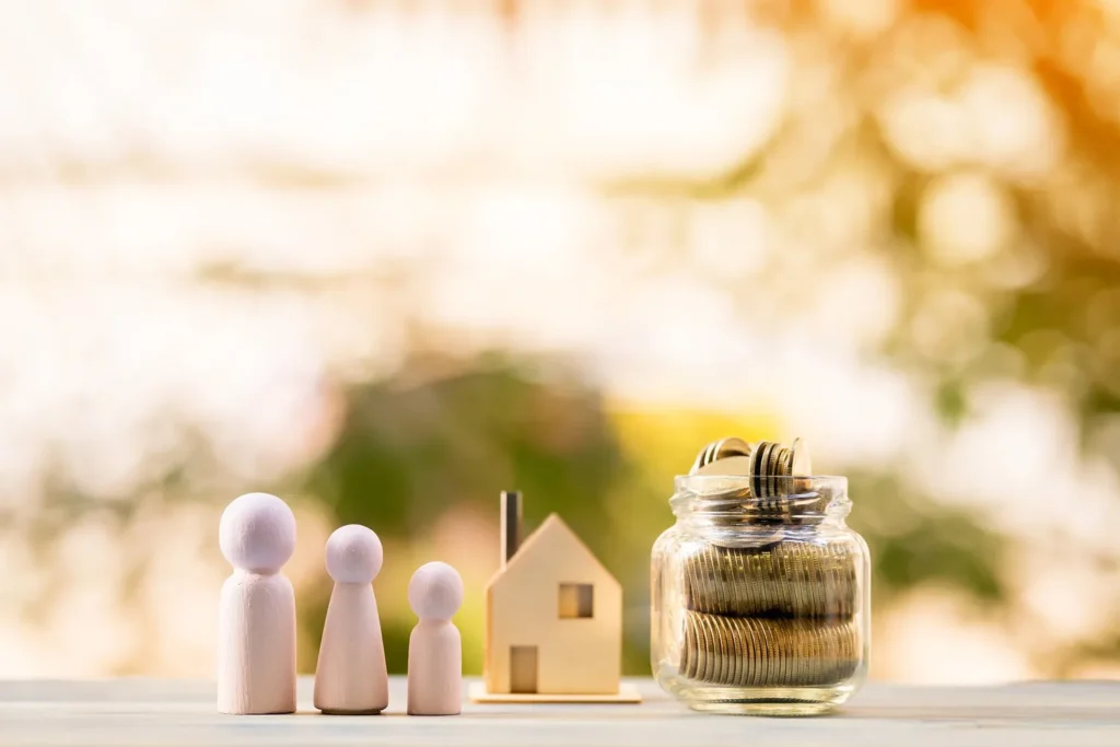 Wooden figures of a family, a house model, and a jar of coins on a table, symbolizing property and finances involved in asset division with a Houston asset division attorney.