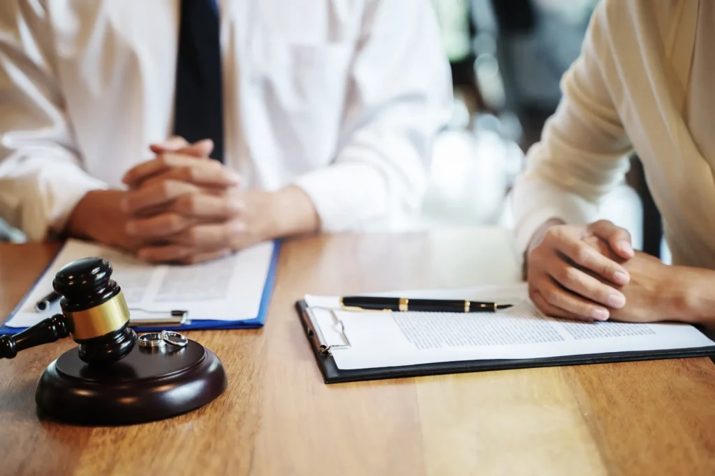 Two people sitting across from each other at a table with legal documents, a gavel, and wedding rings, symbolizing a contested divorce case in Houston.